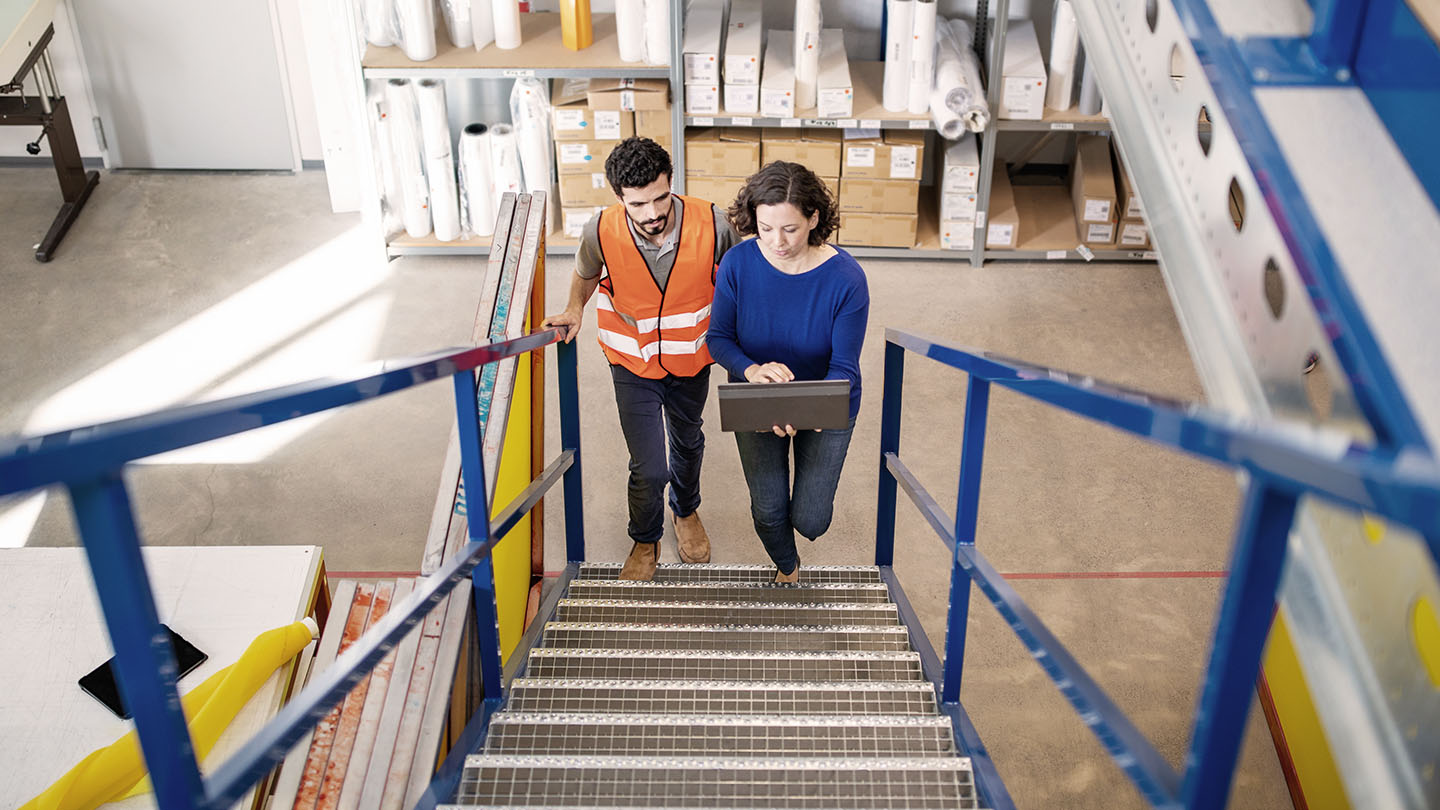 Two people discuss a business loan while walking up stairs in a warehouse
