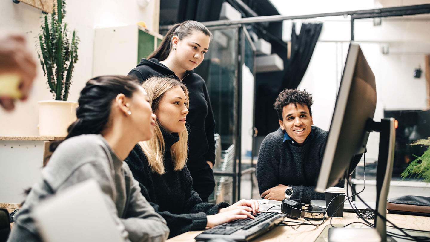 4 people looking a computer screen banner