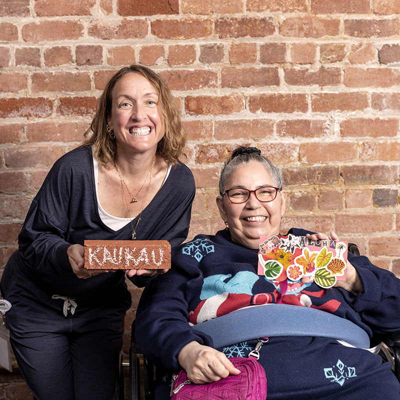 Two women holding a brick saying kaukau