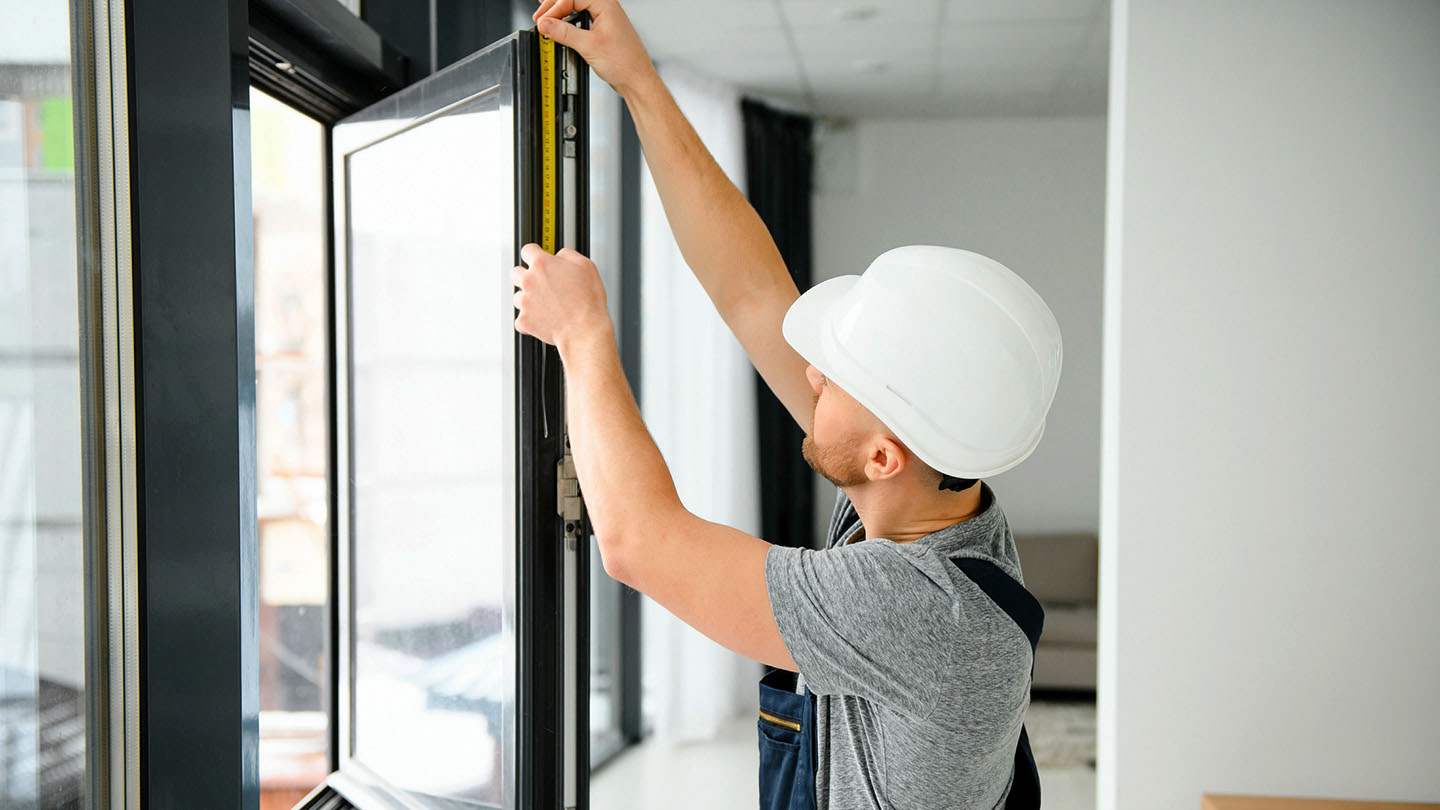 A window installer measures a new window in an apartment unit.