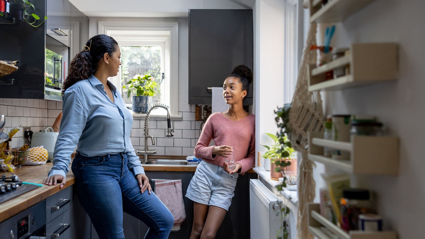 Happy mother and daughter bonding at home in the kitchen and talking - family concepts