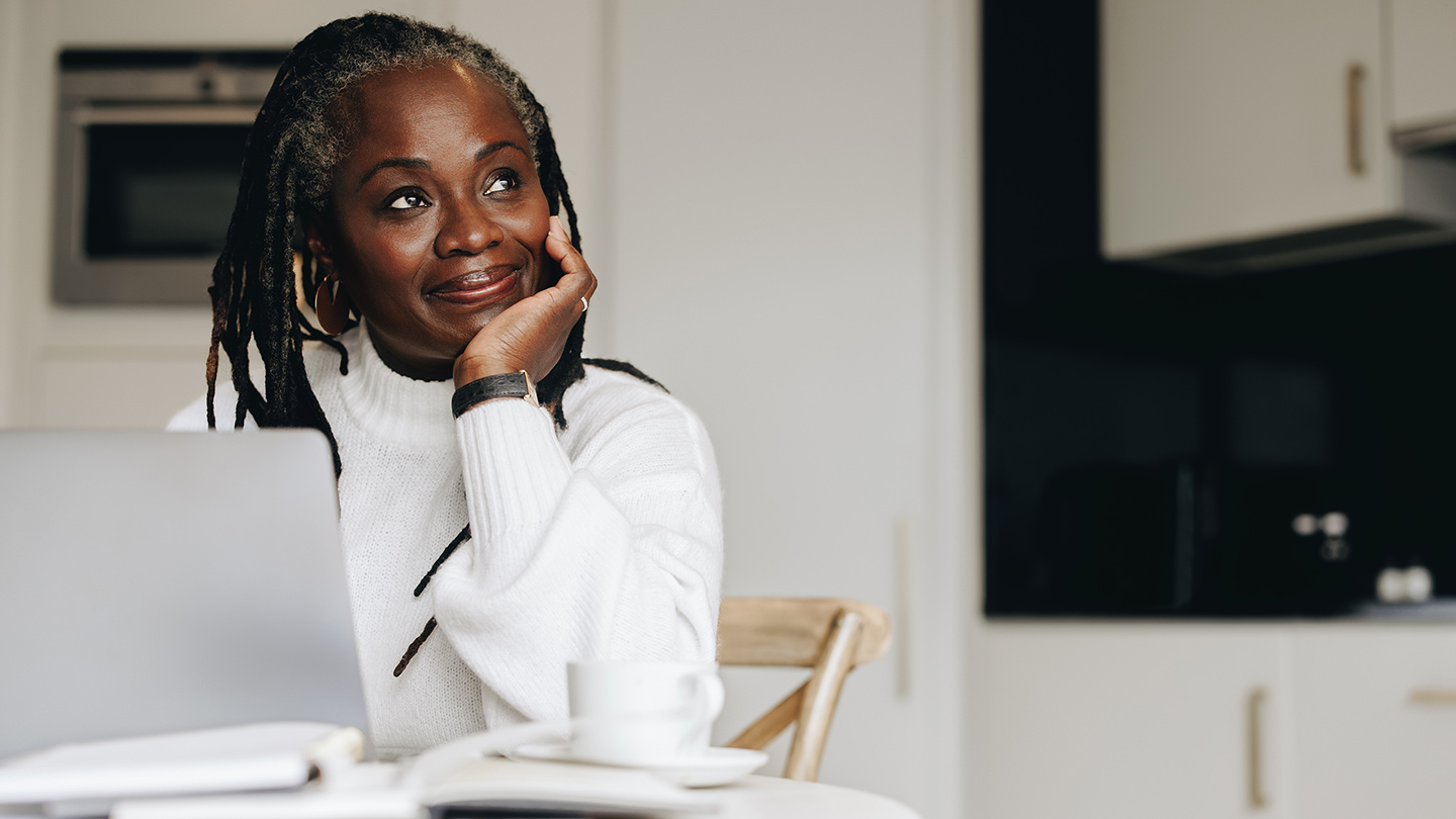 Mature businesswoman looking away thoughtfully while working on a laptop at home. Senior businesswoman doing online freelance work in her home office.