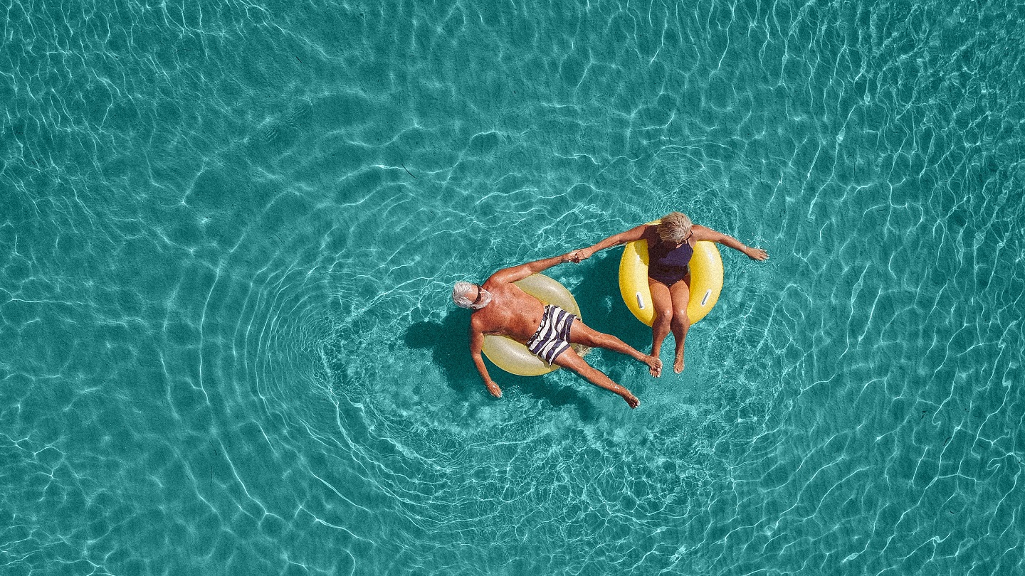 High angle view photo of a senior couple floating in the ocean while using swimming and floating devices