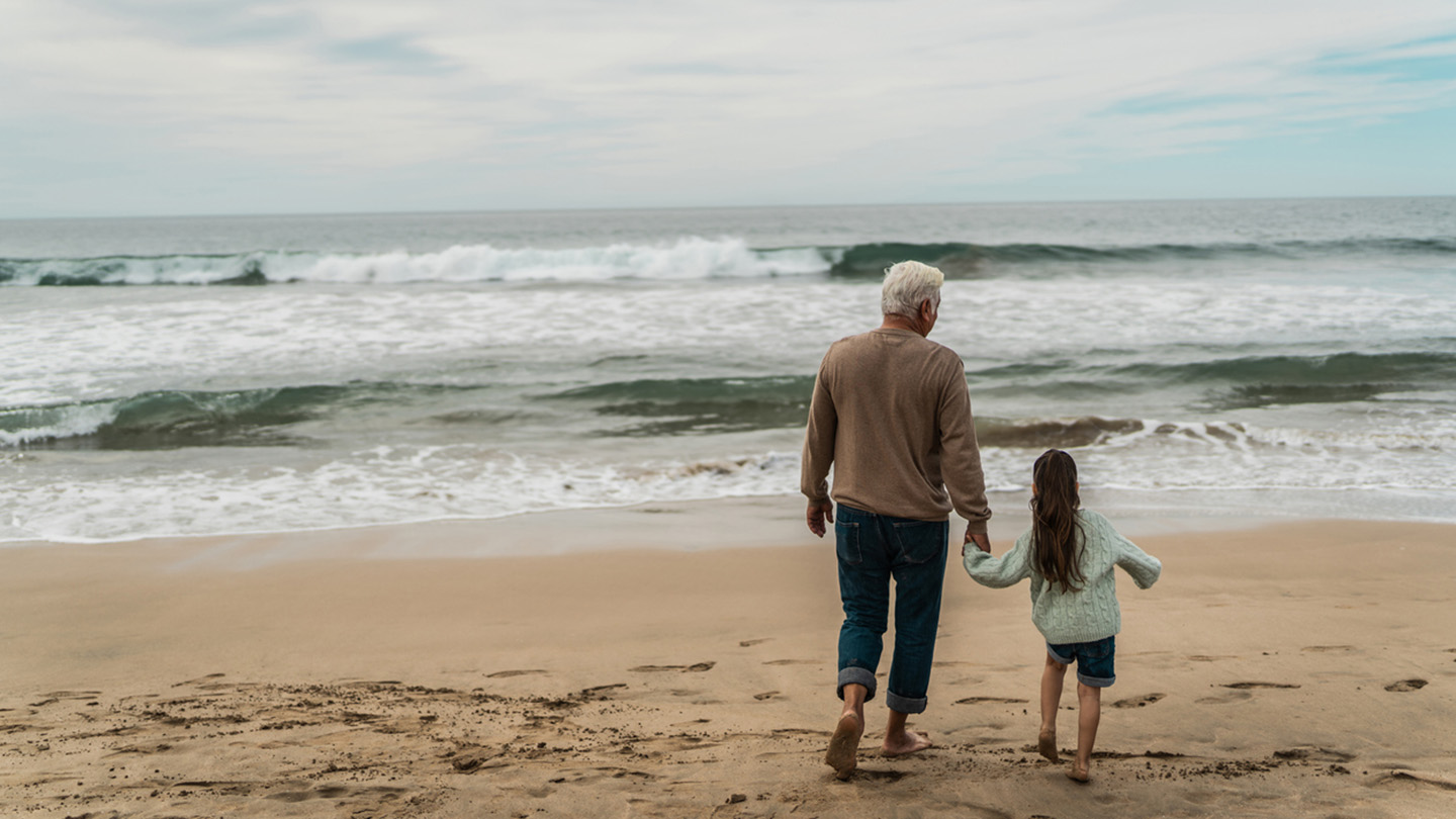 Grandfather talking and walking with granddaughter at beach