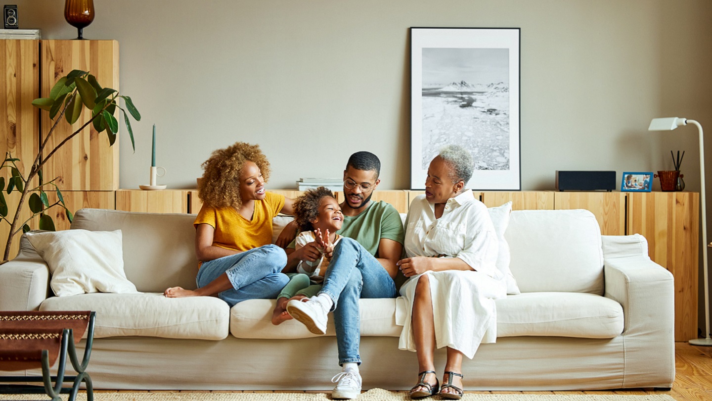 Cheerful boy with parents and grandmother on sofa. Happy family is enjoying in living room. They are spending leisure time together.