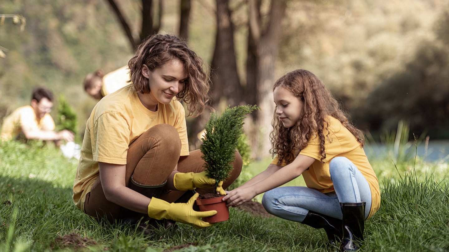 Young mother and little girl planting a tree by river