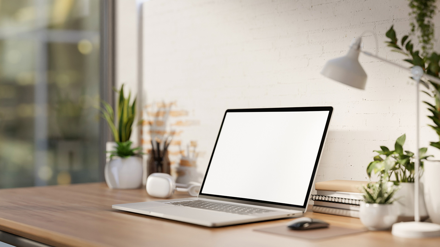 A minimalist workspace features a white-screen laptop computer mockup, headphones, a table lamp, and potted plants on a wooden desk against the white brick wall. a side view 3d render, 3d illustration