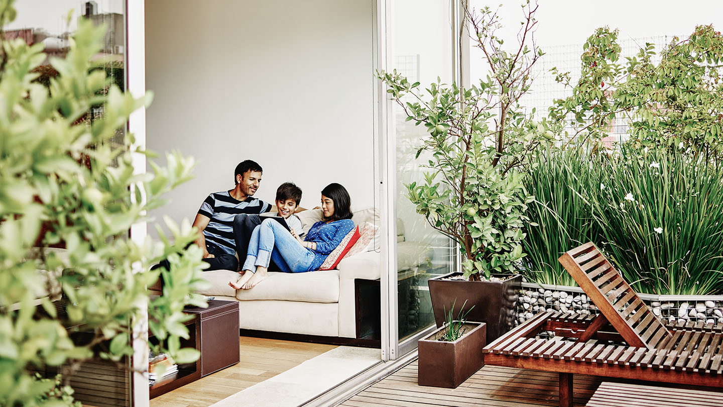 Smiling family sitting together on sofa in home looking at digital tablet