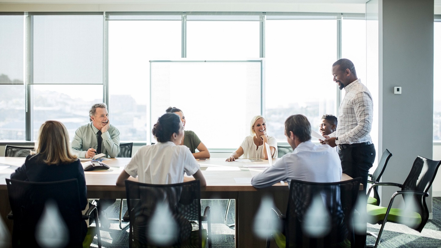 Smiling businessman explaining to colleagues in board room. Multi-ethnic professionals are discussing at conference table during meeting. They are working at office.