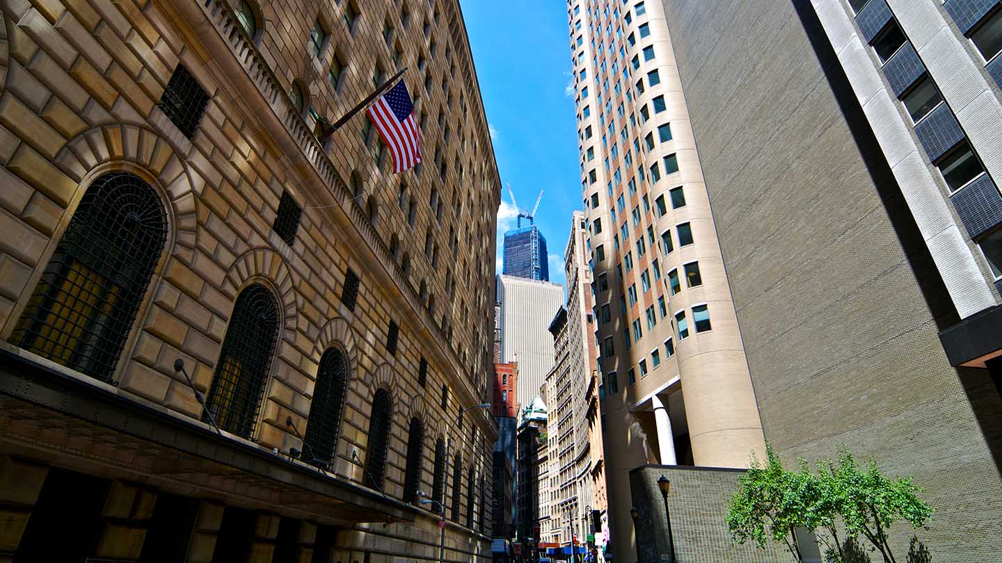 Liberty Street in Manhattan's Financial District with the 22 story 1920's built Federal Reserve Bank of New York Building seen at the left. In the background is One World Trade Center, Lower Manhattan, New York City.