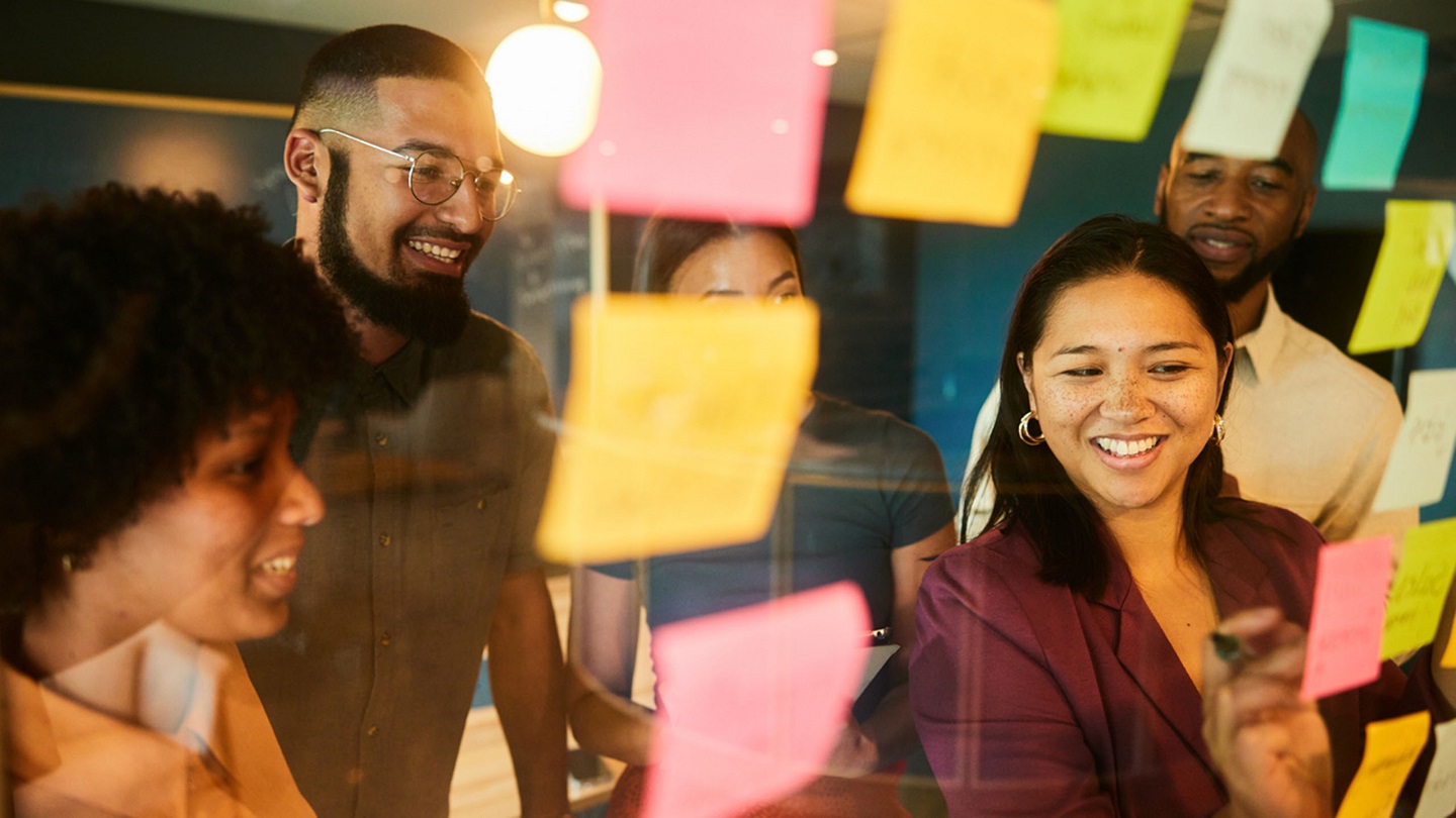 Group of diverse businesspeople smiling during a brainstorming session using adhesive notes on a glass wall in an office